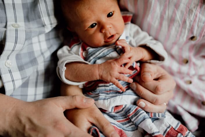 mum and dad are holding baby and baby is looking up. Lovely close up detail of newborn baby. Newborn baby photographer in Hampshire. Newborn baby feet detail shoot. Newborn baby is holding his feet together whilst laying on the bed. Newborn baby photography in Hampshire. Ewa Jones Photography