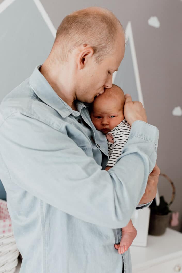 Dad is holding his newborn baby girl close to his chest and he is kissing the baby. Newborn baby photography in Hampshire. Ewa Jones Photography