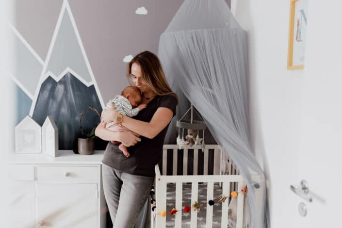 Mum is standing in the newborn baby nursery room and holding her baby girl. Baby girl is sleeping. Newborn photographer in Hampshire. Newborn baby feet detail shoot. Newborn baby is holding his feet together whilst laying on the bed. Newborn baby photography in Hampshire. Ewa Jones Photography