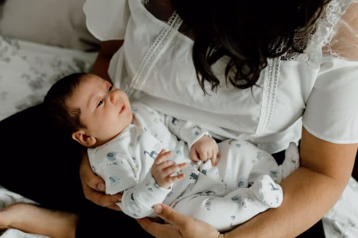 Mum is holding her newborn baby boy and looking down on him. Baby boy is wearing lovely white baby grow with animal prints. Newborn baby photographer in Fleet, Hampshire. Ewa Jones Photography