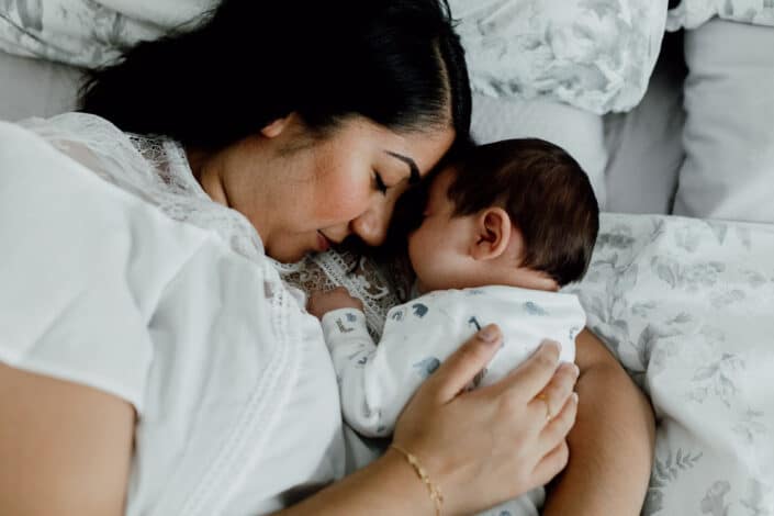 Mum is laying on bed with her newborn baby boy. Baby boy is sleeping and mum has her eyes closed too. Lovely candid photograph of mum and baby first moments. Newborn baby photo session in Fleet, Hampshire. Newborn baby feet detail shoot. Newborn baby is holding his feet together whilst laying on the bed. Newborn baby photography in Hampshire. Ewa Jones Photography