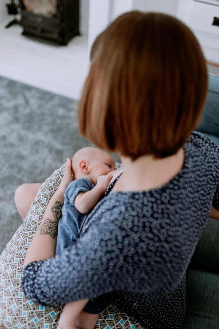 Mum is breastfeeding her newborn baby. Mum is wearing blue dress and baby girl is wearing blue baby grow. Newborn photographer in Hampshire. Ewa Jones Photography