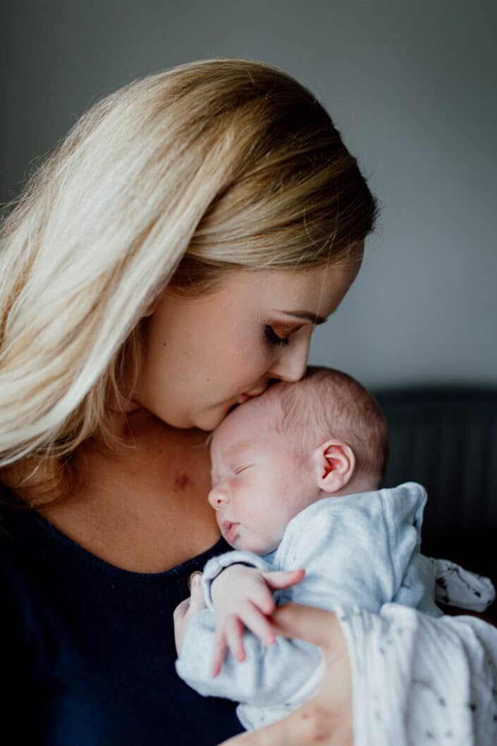 Mum kissing newborn baby next to the window. Natural newborn baby photoshoot in Basingstoke, Hampshire, Ewa Jones Photography