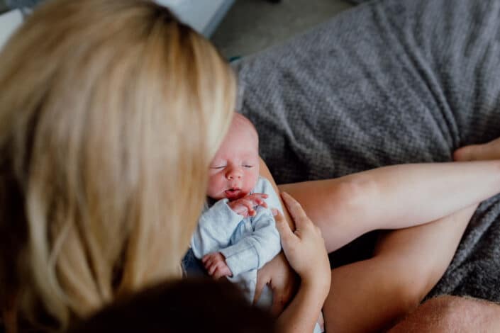 Mum is sitting on the bed and looking down at her little baby boy. Baby boy is sleeping. Lifestyle family photographer in Hampshire. Ewa Jones Photography