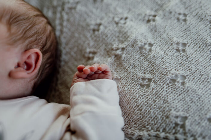 Detail shoot of newborn baby hand. Baby is laying on bed and in shoot you can only see baby's hand. Newborn baby photographer in Basingstoke, Hampshire. Ewa Jones Photography