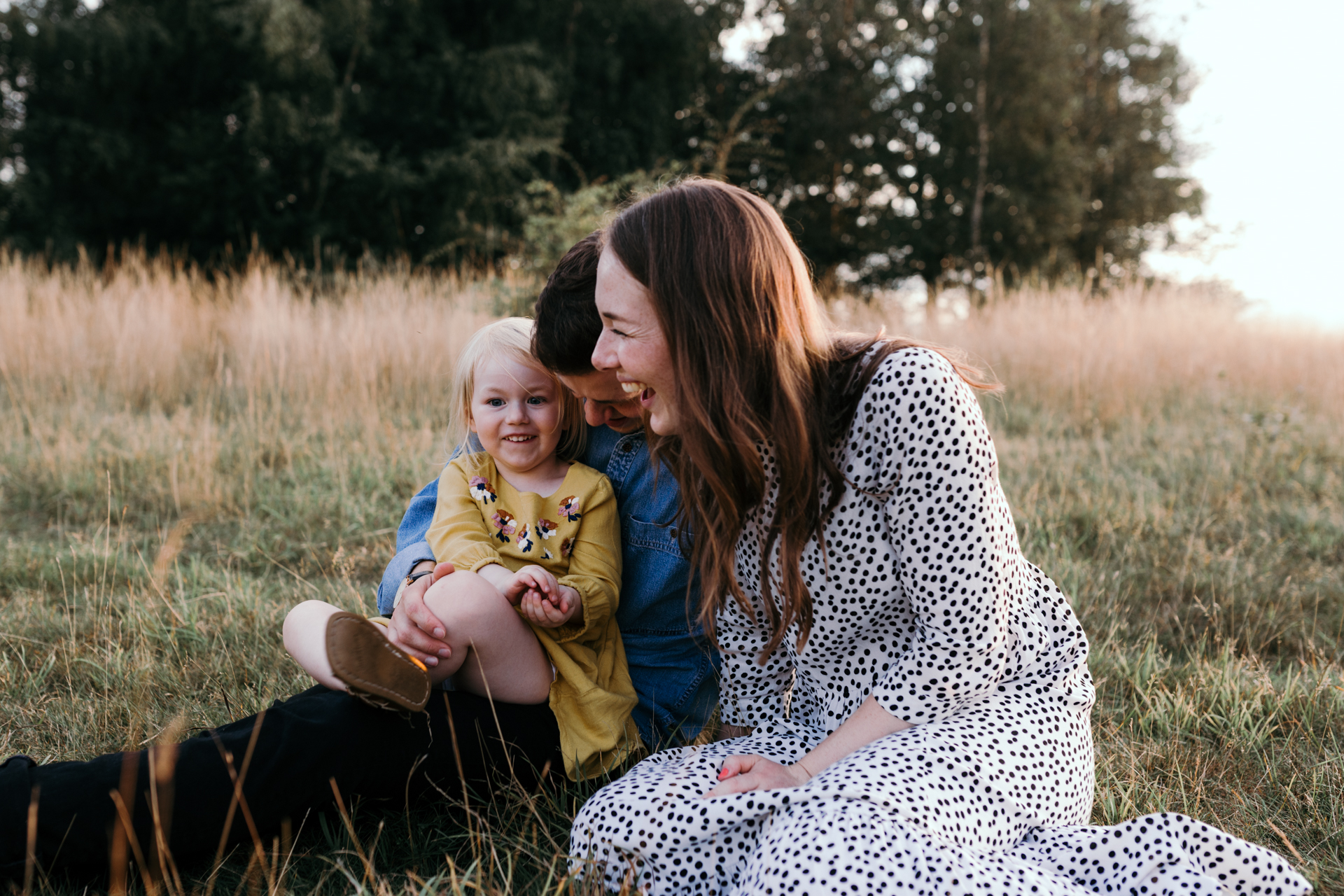 Mum and dad sitting on the grass with daughter. Sunset family photoshoot in Basingstoke. Hampshire. Ewa Jones Photography