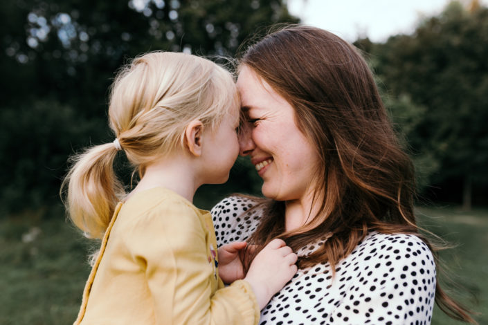 Mum holding a girl in a yellow dress, smiling to her. Sunset family photoshoot in Basingstoke. Hampshire. Ewa Jones Photography