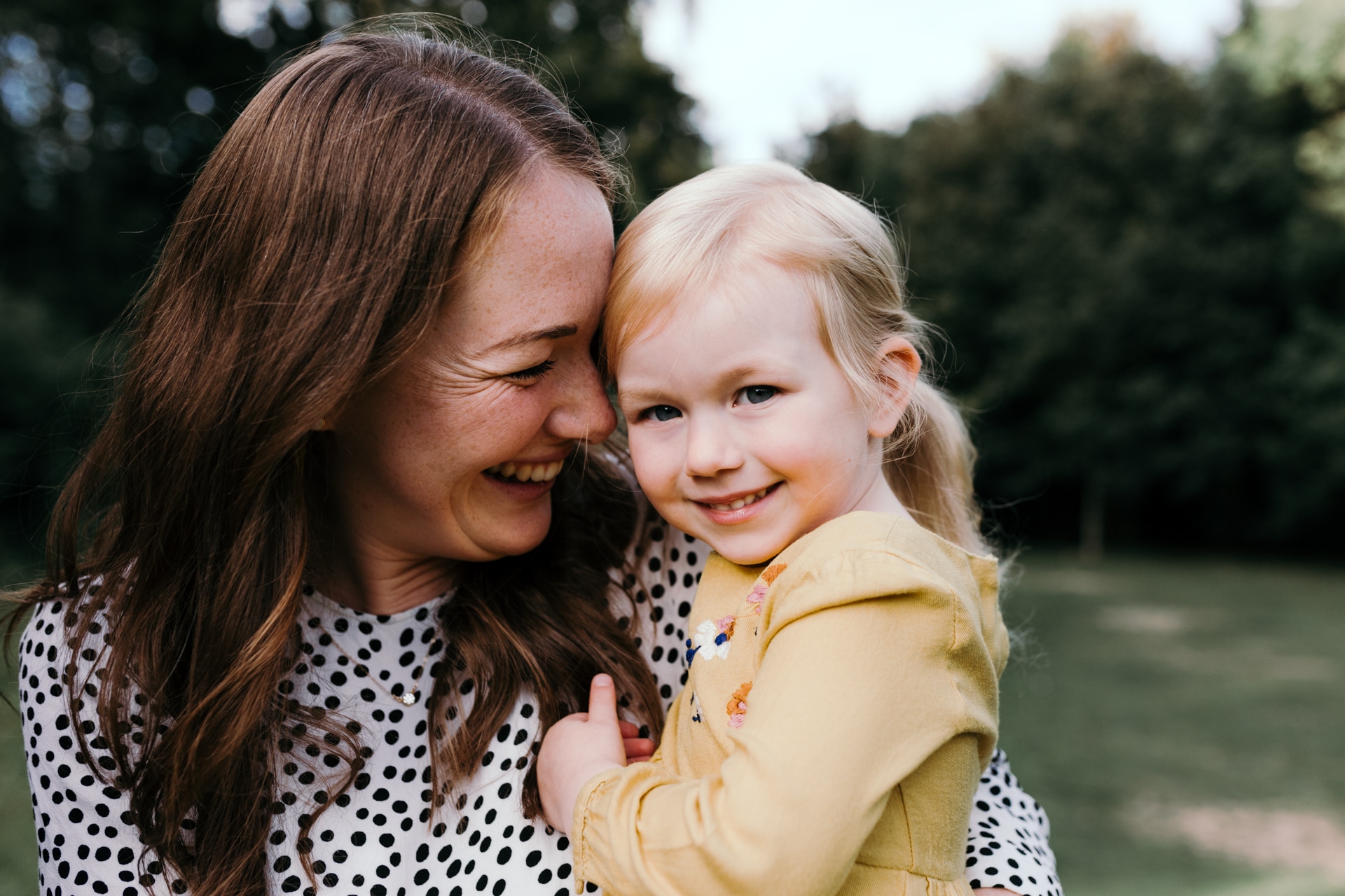 Mum holding a girl in a yellow dress, smiling to her. Sunset family photoshoot in Basingstoke. Hampshire. Ewa Jones Photography