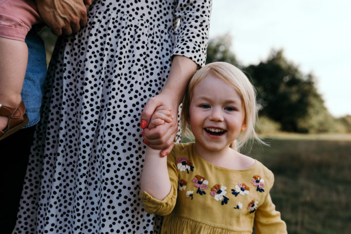 Happy girl holding onto mums hand in the fields. Sunstet family photoshoot in Basingstoke.  Ewa Jones Photography