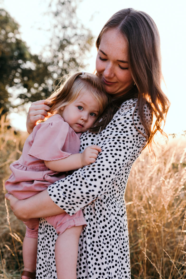 Mum is holding a girl in the field. Back lit photography. family photoshoot in Basingstoke. Ewa Jones Photography