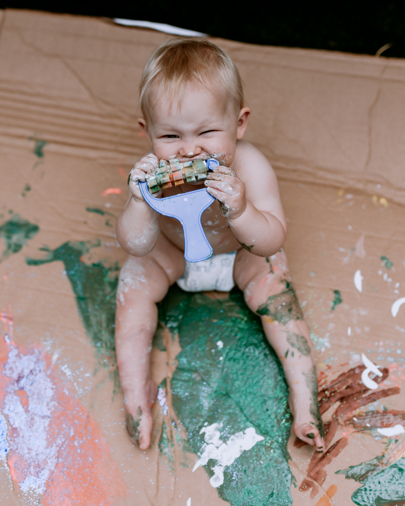 Girl playing with paint and eating paint brush by Ewa Jones Photography