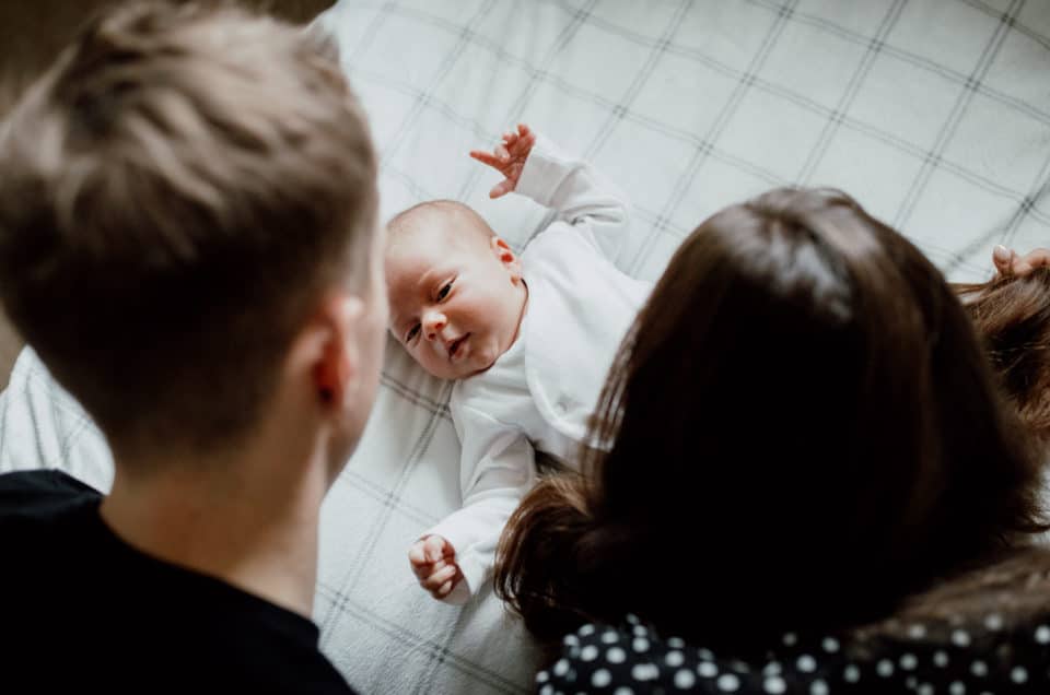 Mum and dad looking at the newborn baby on the bed. Newborn videography