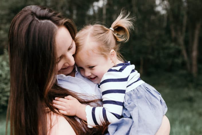 Girl is cuddling tight to her mum. Girl is wearing a stripy dress and have pony tails. Mum is lovingly looking at her daughter. Family photography in Basingstoke. Ewa Jones Photography