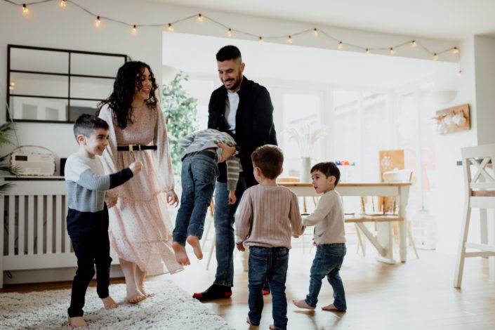 Mum and dad are dancing in the kitchen with their four boys. Dad is lifting up one boy. Other boys are dancing and laughing. Family lifestyle photographer in Hampshire. Ewa Jones Photography