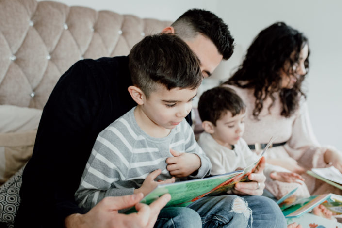 Boy is reading a dinosaur book and sitting on daddy's lap. Izzo family. Ewa Jones Photography