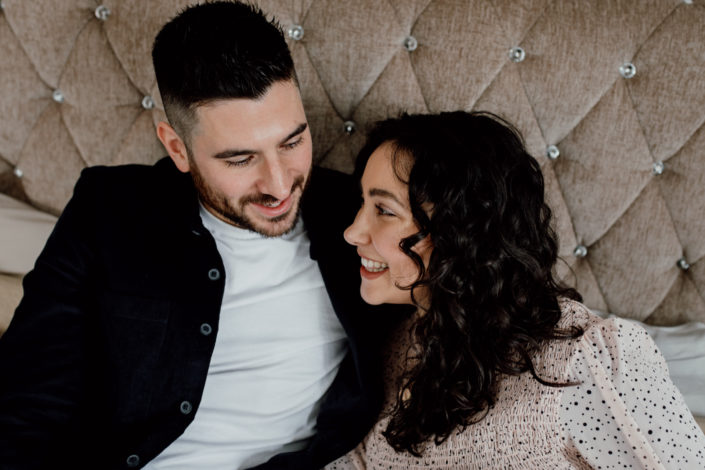 Mum and dad are sitting close on the bed. Both are looking at each other and smiling to each other. Family lifestyle photography in Hampshire. Ewa Jones Photography