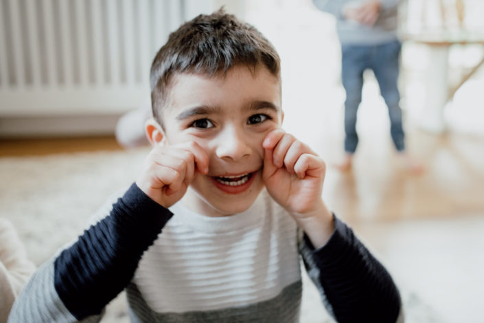 Boy is laughing and holding his hands on his cheeks. Family lifestyle photographer in Hampshire. Ewa Jones Photography