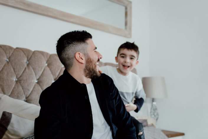 Dad and son are sitting on the bed and laughing at each other. Candid family moment. Izzo Family. Ewa Jones Photography