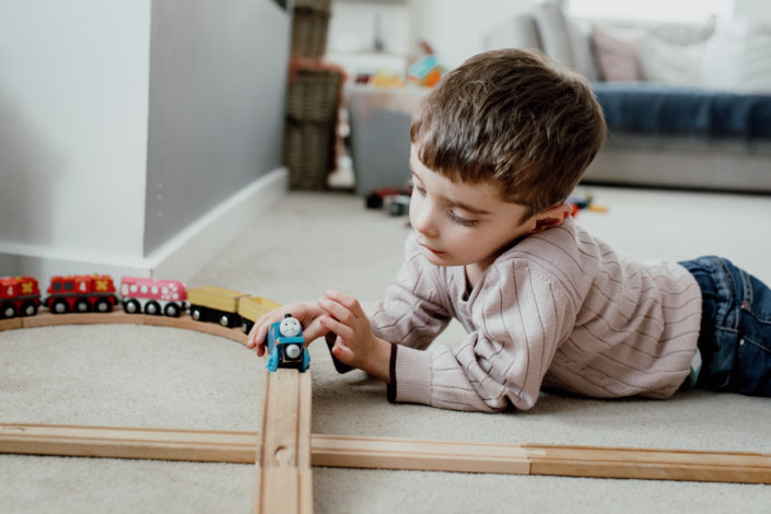 Boy is laying on the floor and playing with trains and train track. Family photography. Izzo Family. Ewa Jones Photography