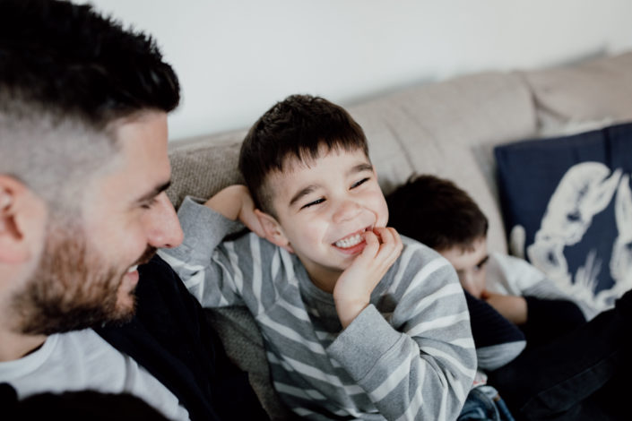 Dad is looking at his son and boy is smiling. Boy is wearing grey stripy jumper. Family photographer in Hampshire. Ewa Jones Photography