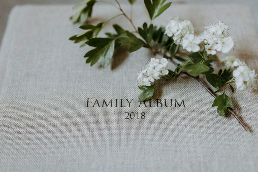 Photo album in light grey textile finish with a white flower laying on the album. Words on the album are saying Family Album 2018. Family photography in Basingstoke. Ewa Jones Photography