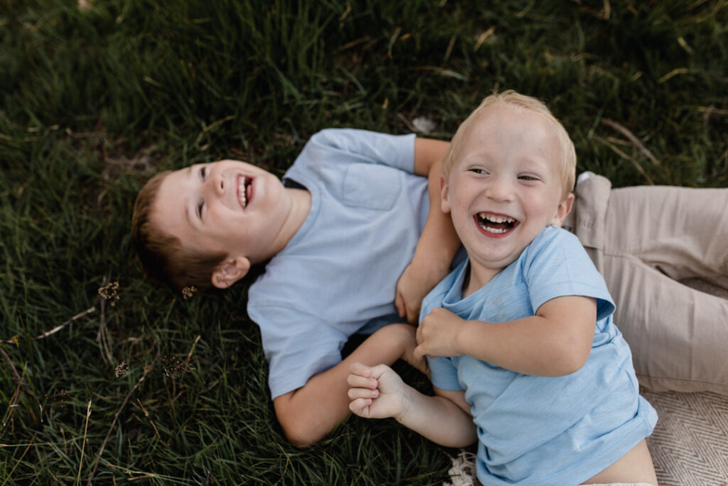 Two boys are laying on the grass and laughing. Brothers candid photography. Family lifestyle photography in Hampshire. Ewa Jones Photography