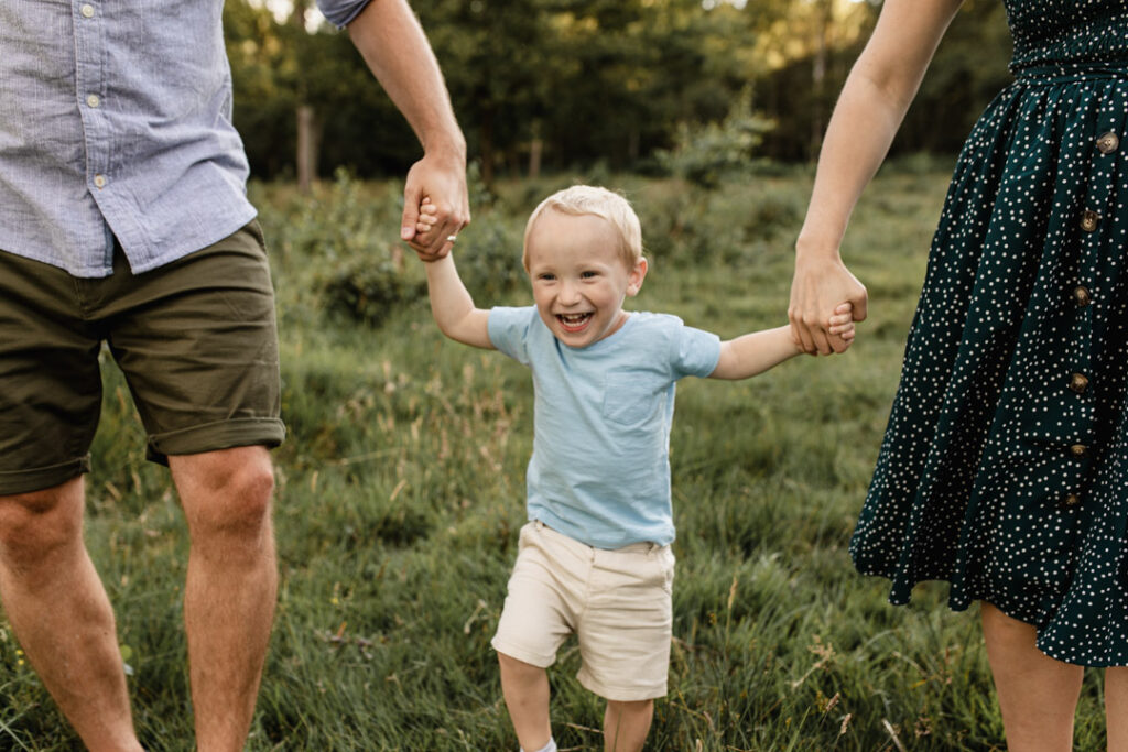 Little boy id holding parents hands. He is happy and smiling. Family photographer in Basingstoke. Ewa Jones Photography