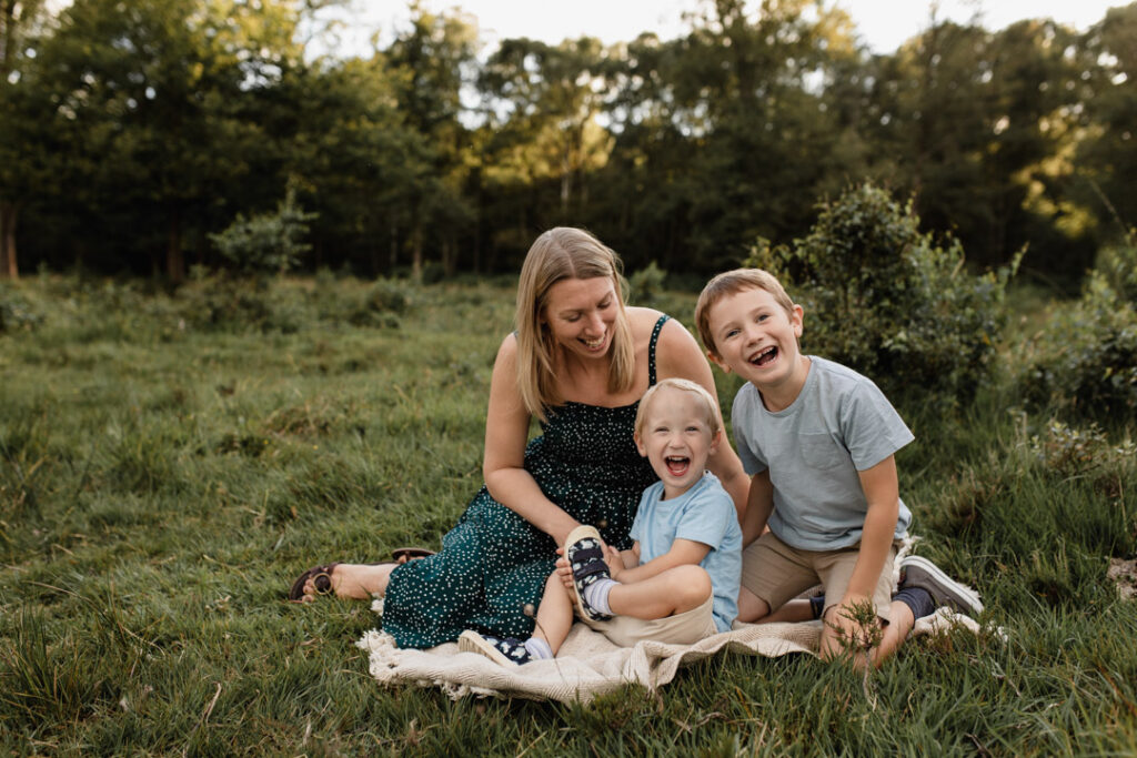 Mum and two boys are sitting on the blanket and laughing. Lovely family photography in Hampshire. Ewa Jones Photography