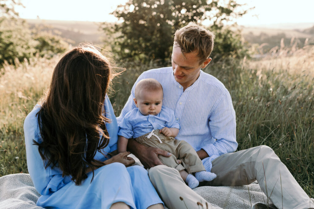 Mum and dad are sitting on the grass and both looking at their baby. Lovely candid family moment. family photography in Basingstoke. Ewa Jones Photography