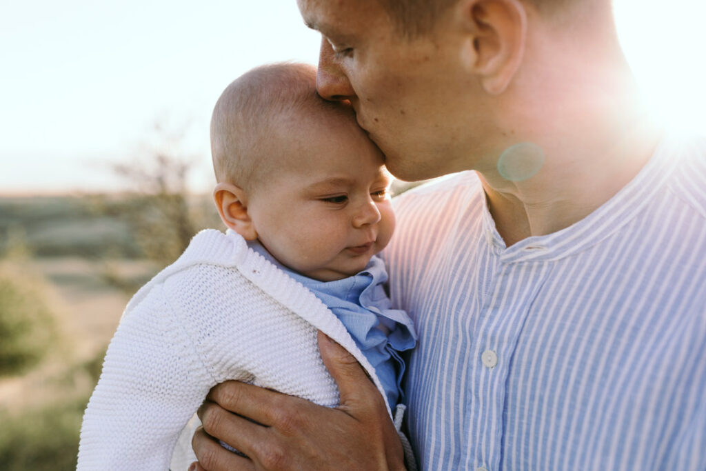 Sunset family photo session - Family photography - Ewa Jones Photography-14 Dad is kissing a little boy on his forehead. Dad has his eyes closed. Salisbury photo session in the hills.Lovely family photo session. family photographer in Basingstoke. Ewa Jones Photography