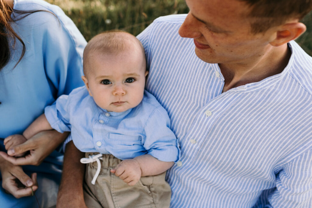 Little baby boy is looking at the camera and holding his mum hand. Family sunset photo session. family photographer. Ewa Jones Photography