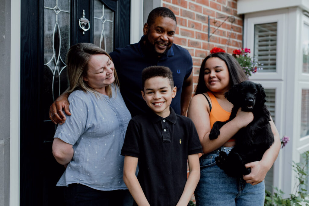 Family of four is standing in front of the house. Family doorstep photo sessions. Ewa Jones Photography