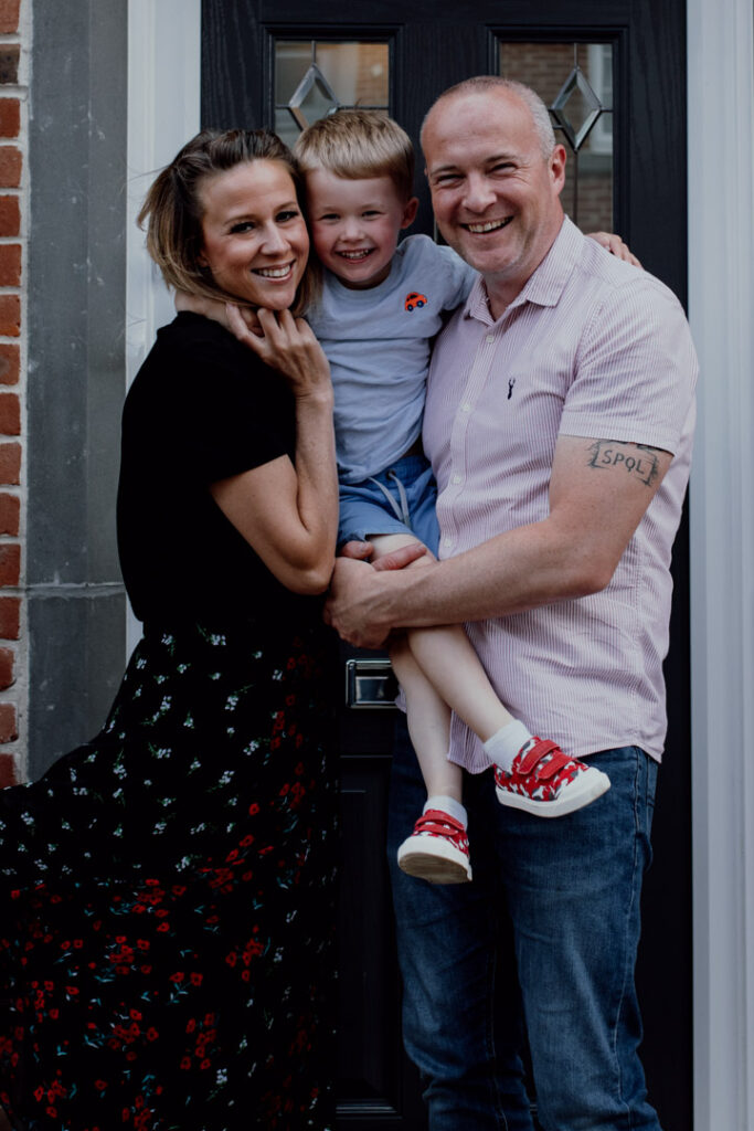 Mum and dad are holding their son and smiling. family doorstep photo sessions. Family photographer in Basingstoke. Ewa Jones Photography