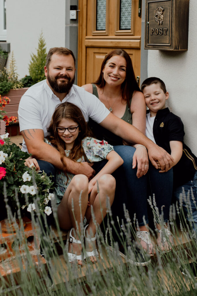 Family is sitting on their front step and smiling. Family photo session in Basingstoke. Ewa Jones Photography