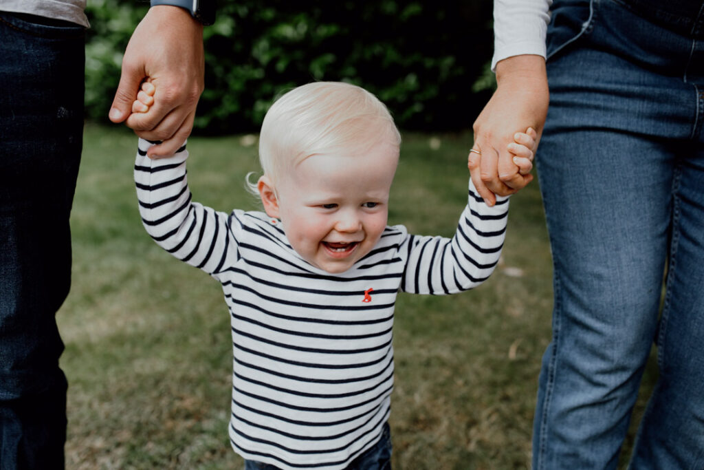 Little boy is smiling and holding his mum and dad hand. family lifestyle photography in Hampshire. Ewa Jones Photography