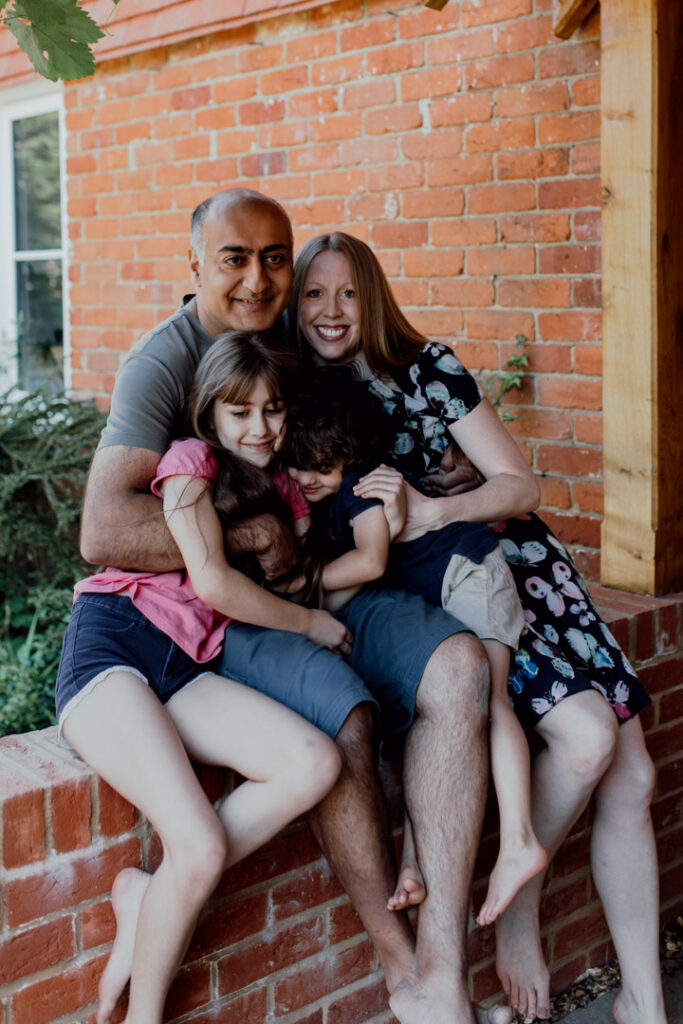 Family is sitting on the wall in their front garden and cuddling to each other. family doorstep photo sessions. family photographer in Hampshire. Ewa Jones Photography