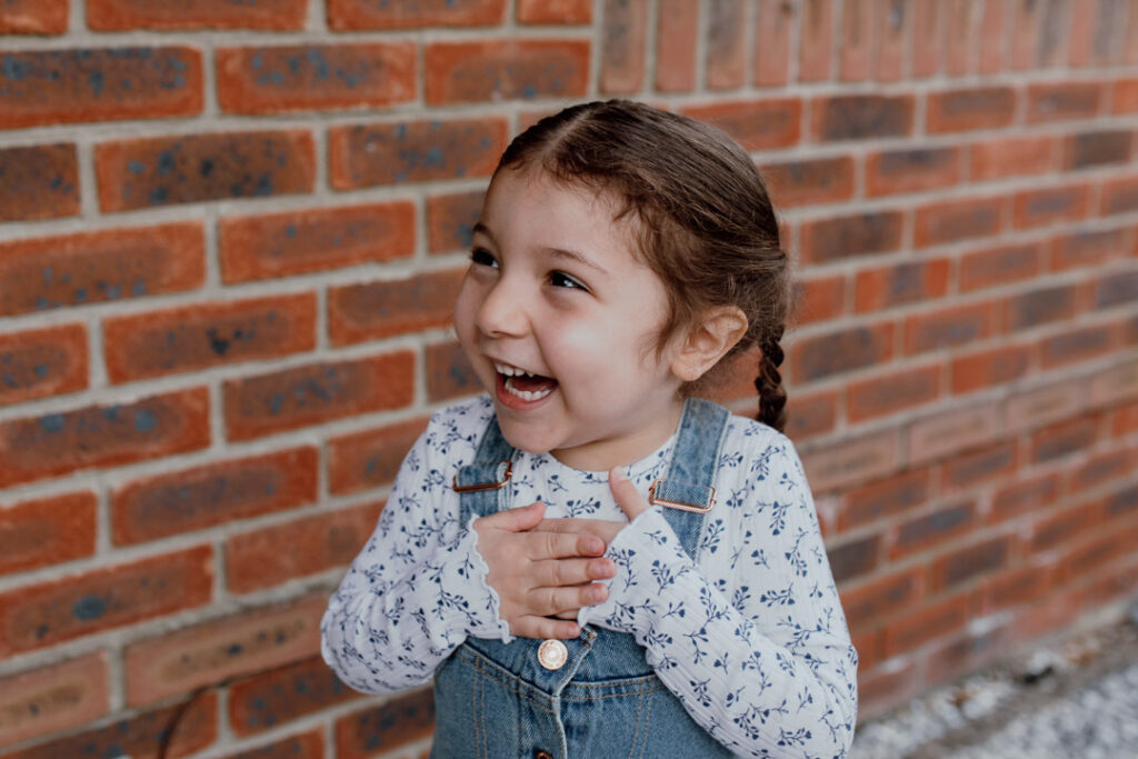 Girl is laughing and looking at her mum. She is holding her hands together. Lovely candid photograph. Lifestyle photography in Basingstoke. Ewa Jones Photography