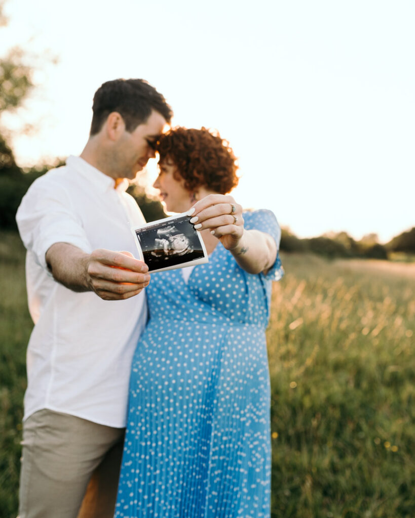 Expecting parents are holding their baby scan. They are standing infront of the sun. Lovely sunset photography in Hampshire. Ewa Jones Photography