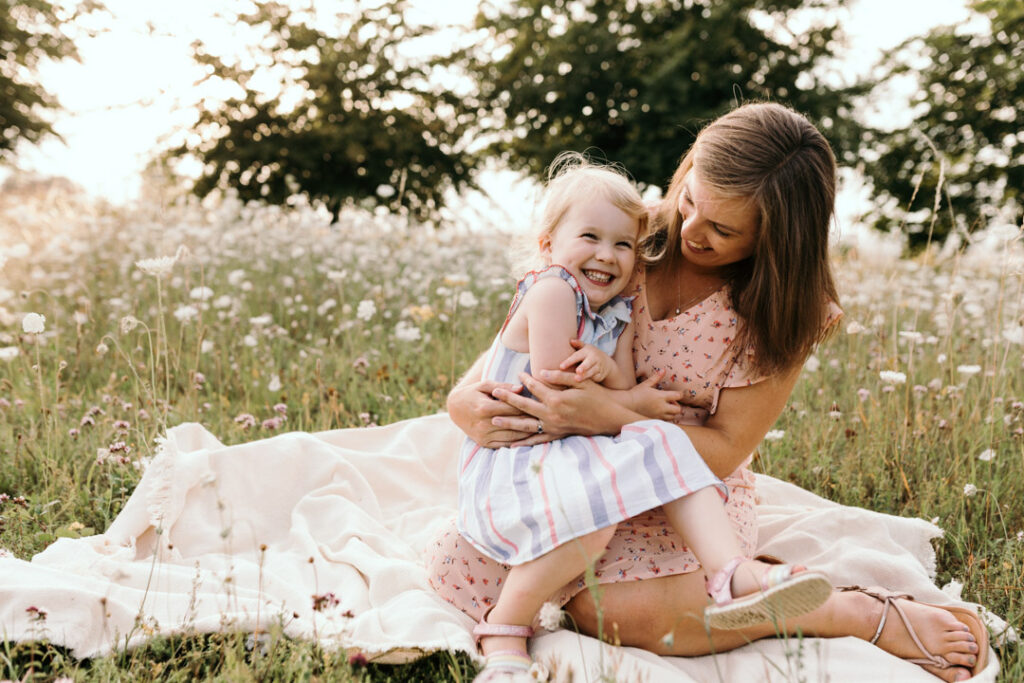 Mum and daughter are sitting on the blanket and laughing. Lovely sunset family photo session in Basingstoke. Ewa Jones Photography