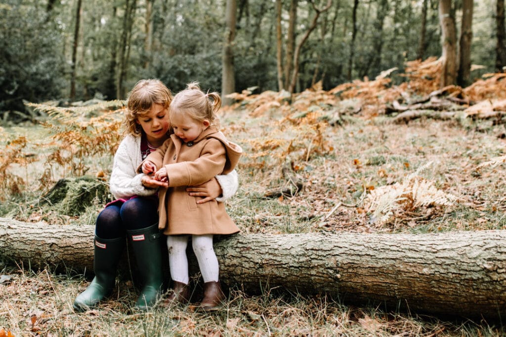 Two girls are sitting on the log and looking at the acorns. Autumn family photography in Hampshire. Ewa Jones Photography