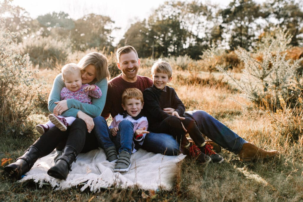 Family of 5 is sitting on the grass and laughing. Autumn family sunset session. Family photography in Hampshire. Ewa Jones Photography