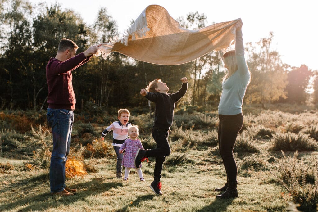 Mum and dad are holding the blanket and kids are running through the blanket. Lovely autumn family photography in Hampshire. Ewa Jones Photography