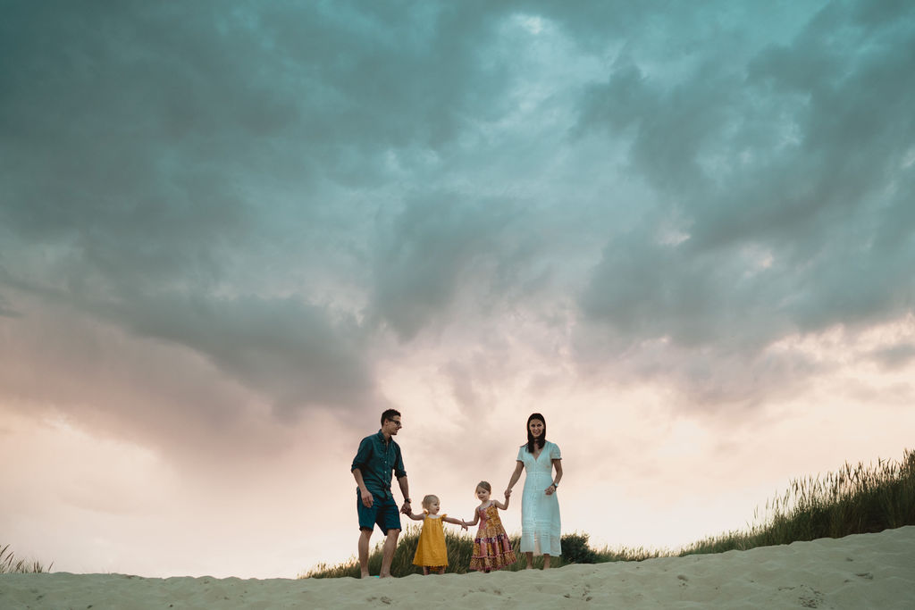 Family is standing at the top of the sandy dunes. Lovely sunset family photography