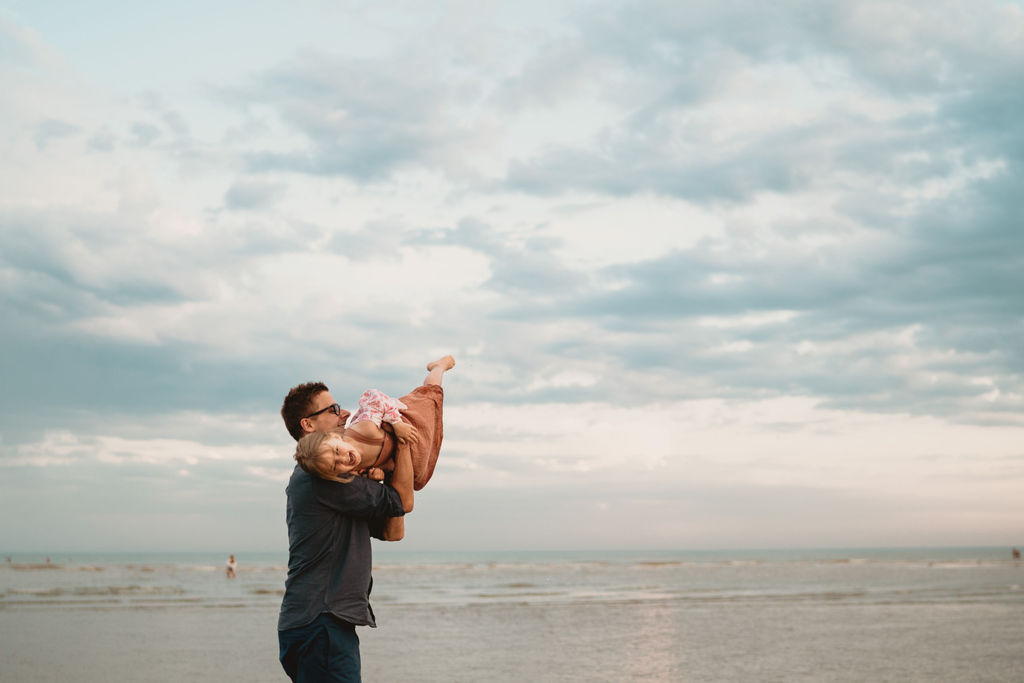 Dad is lifting little girl in the air. Family photo session