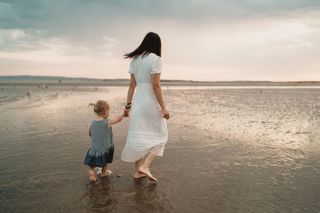 Mum and daughter are holding hands and walking on the beach. Lovely family photo session