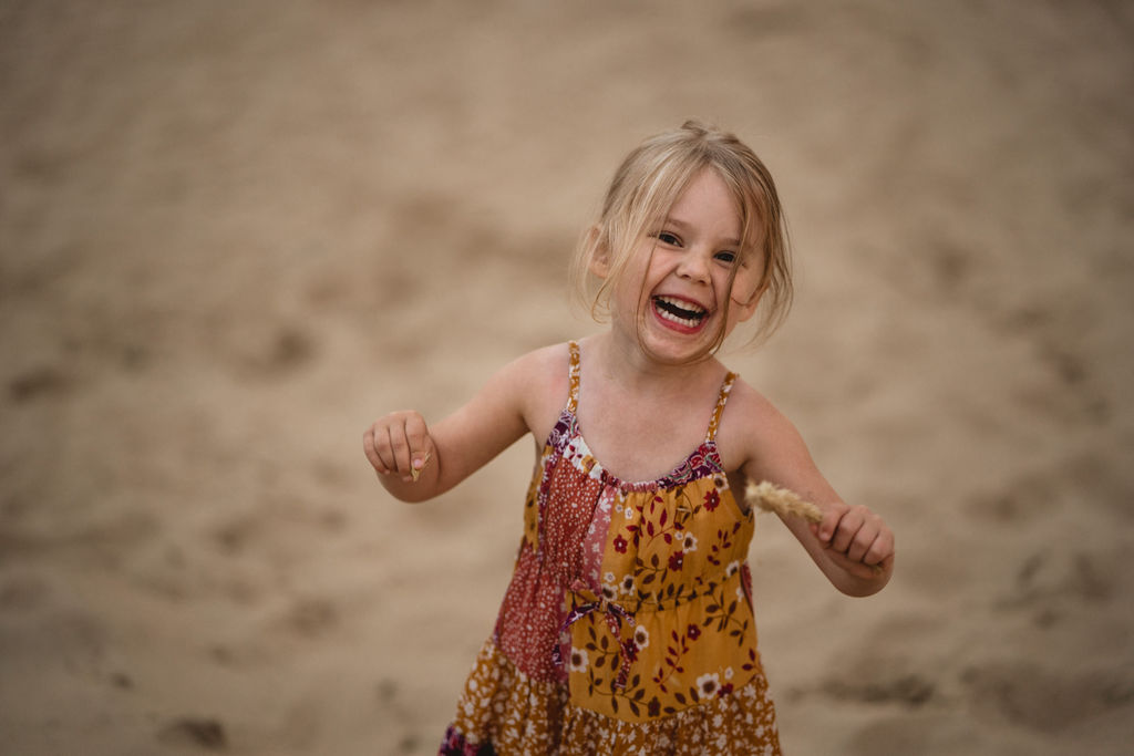 Little girl is smiling to the camera. She is wearing lovely colorful dress. Family photo session