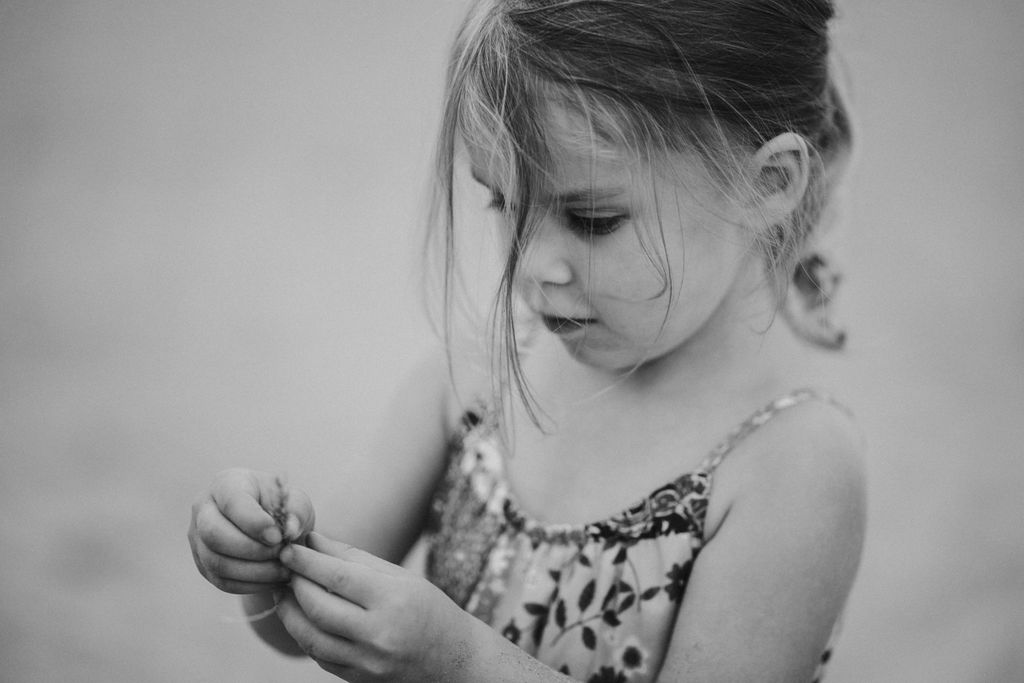 Little girl is holding a grass in her hands. Candid close up photo