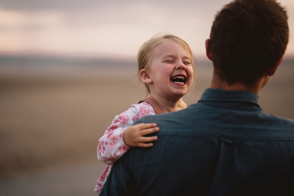 Little girl is laughing and dad is looking at her. Family photo session