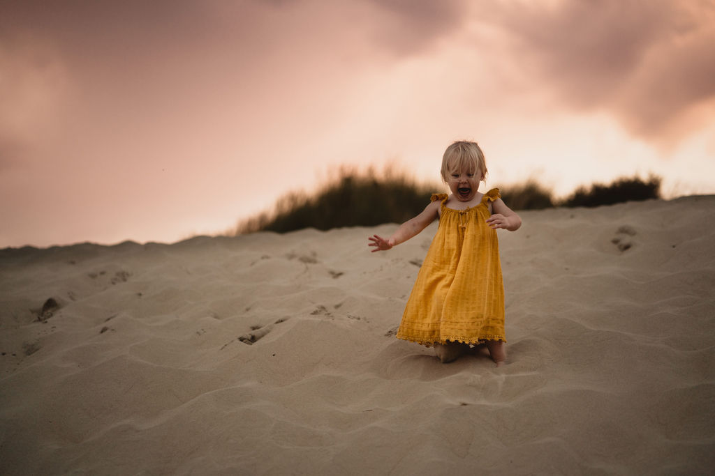 Little girl is running down on the sand dunes. Lifestyle family photography