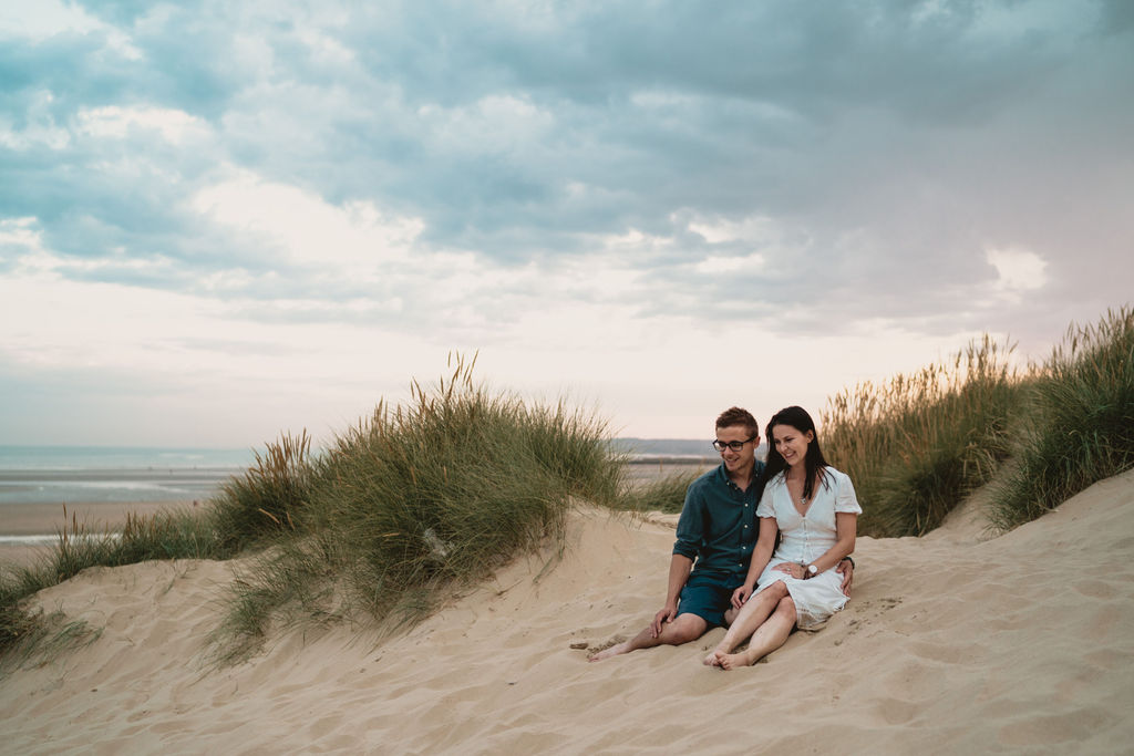 Man and woman are sitting on the sandy dunes. Lifestyle family photography